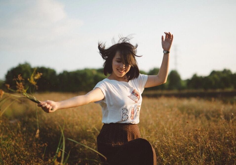 A woman in the middle of a field with her arms outstretched.