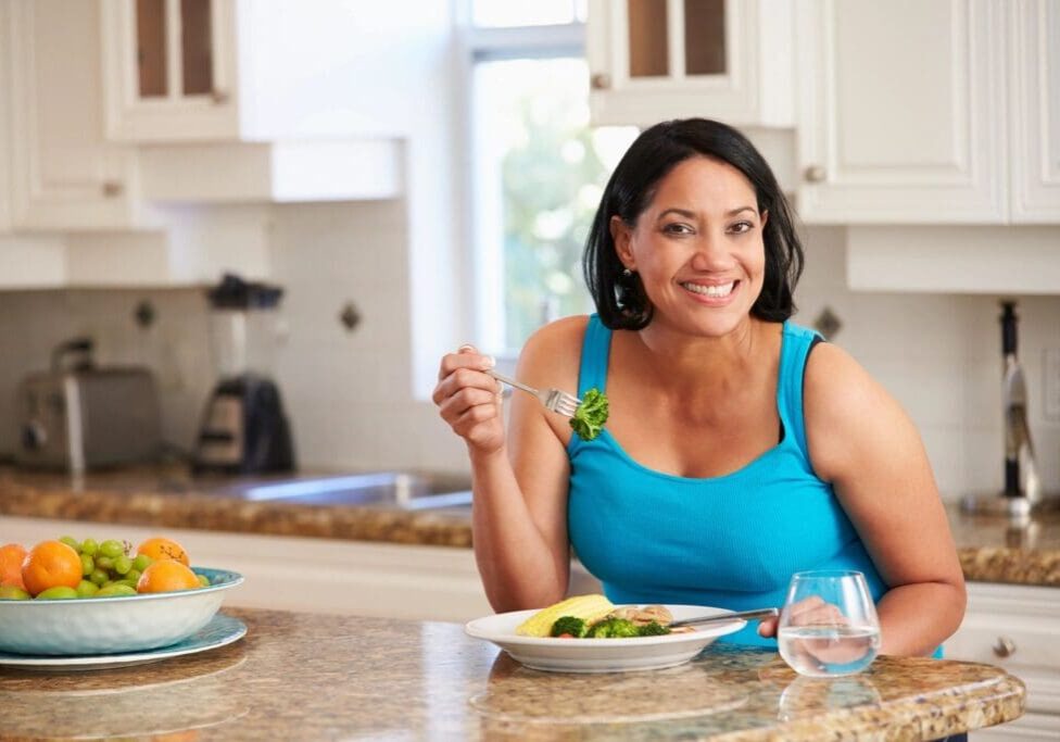 Smiling woman eating vegetables at kitchen counter